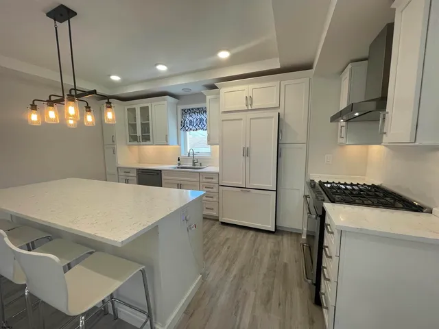 a kitchen with a white center island a stove a refrigerator cabinets and wooden floor