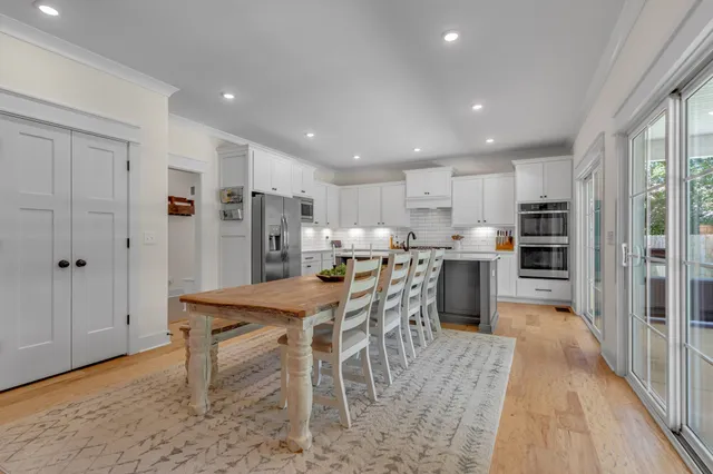 a kitchen with stainless steel appliances granite countertop a refrigerator a sink dishwasher a stove and a dining table with wooden floor