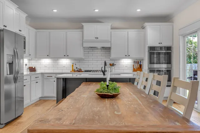 a kitchen with stainless steel appliances granite countertop a stove a sink a refrigerator and a dining table with wooden floor