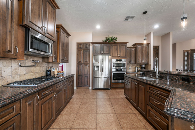 2376 Stone Crest Circle St. George, UT 84790 - Photo 11 of 61 Kitchen with dark stone counters, dark wood finish cabinetry, stainless steel appliances, and a textured ceiling