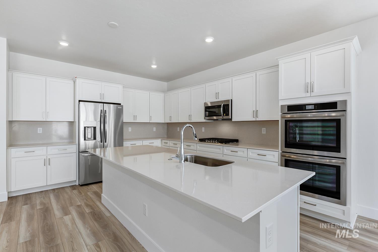 4548 West Wapoot Street Meridian, ID 83646 - Photo 9 of 17 Kitchen featuring a central island with an undermount sink, white cabinetry, integrated stainless steel appliances, and wood-finish flooring