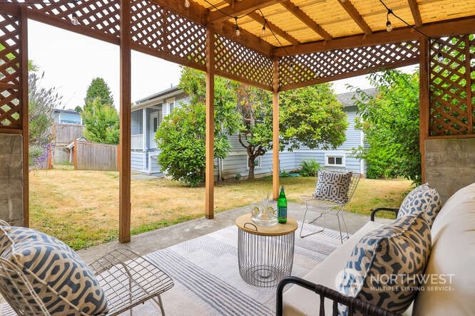 9340 45th Avenue Southwest Seattle, WA 98136 - Photo 21 of 33 a view of a patio with couches chairs dining table and chairs barbeque grill with a small yard and large trees