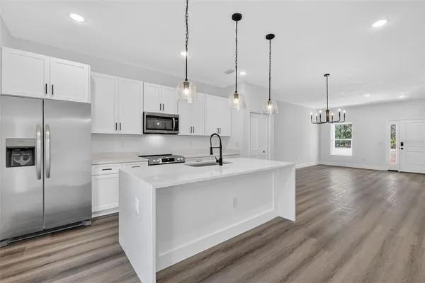 a kitchen with stainless steel appliances granite countertop a sink a stove a refrigerator and white cabinets with wooden floor