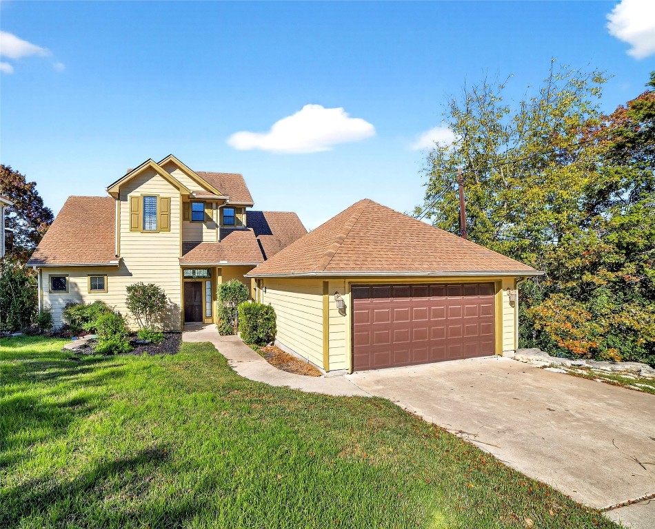 Traditional-style house with a shingled roof, a garage, a front yard, and driveway
