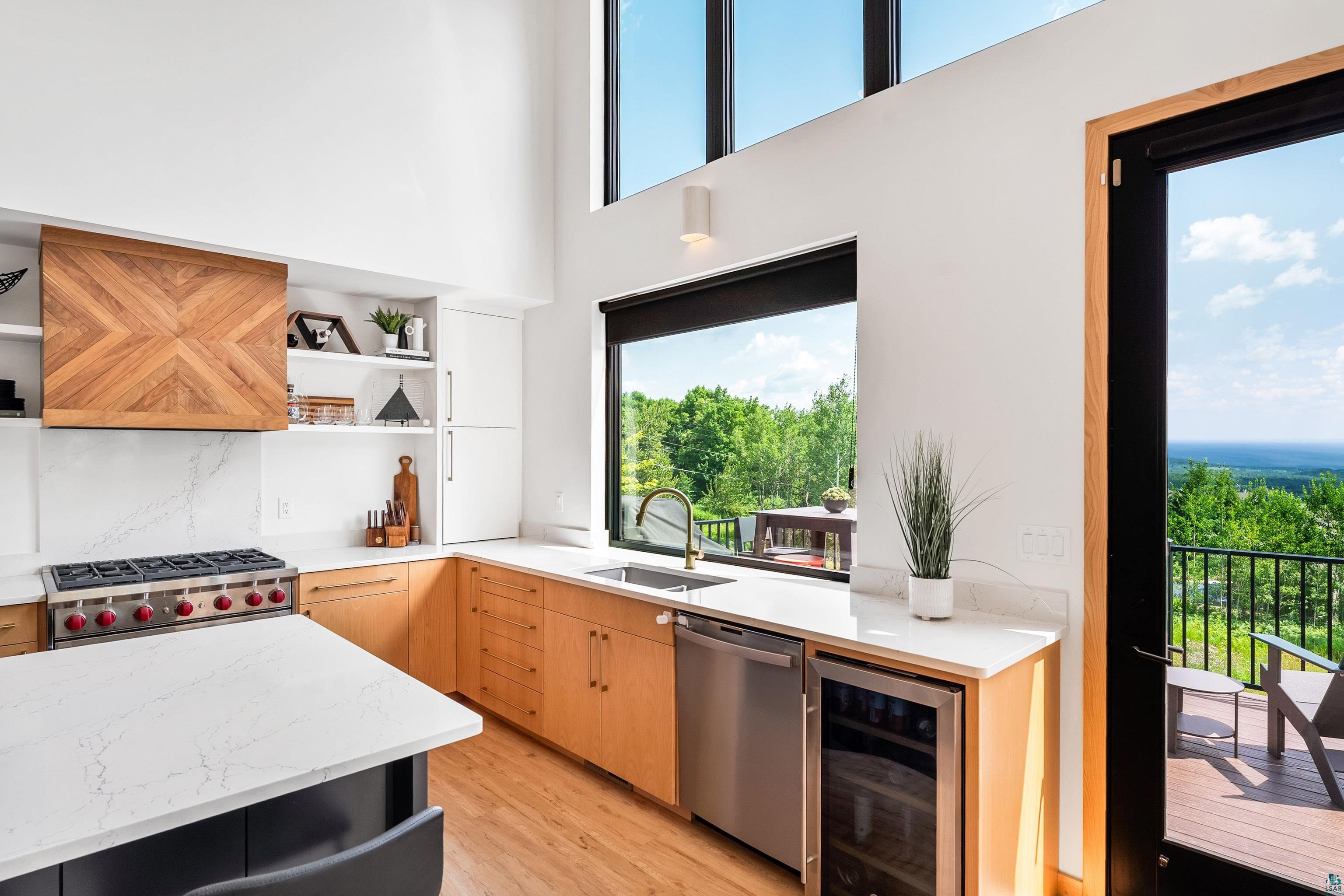 814 Pleasant View Road Duluth, MN 55803 - Photo 14 of 49 Modern kitchen featuring vaulted ceilings, a built-in gas range with a decorative wood hood, light-toned wood-finish cabinetry, a beverage cooler, and access to an outdoor deck