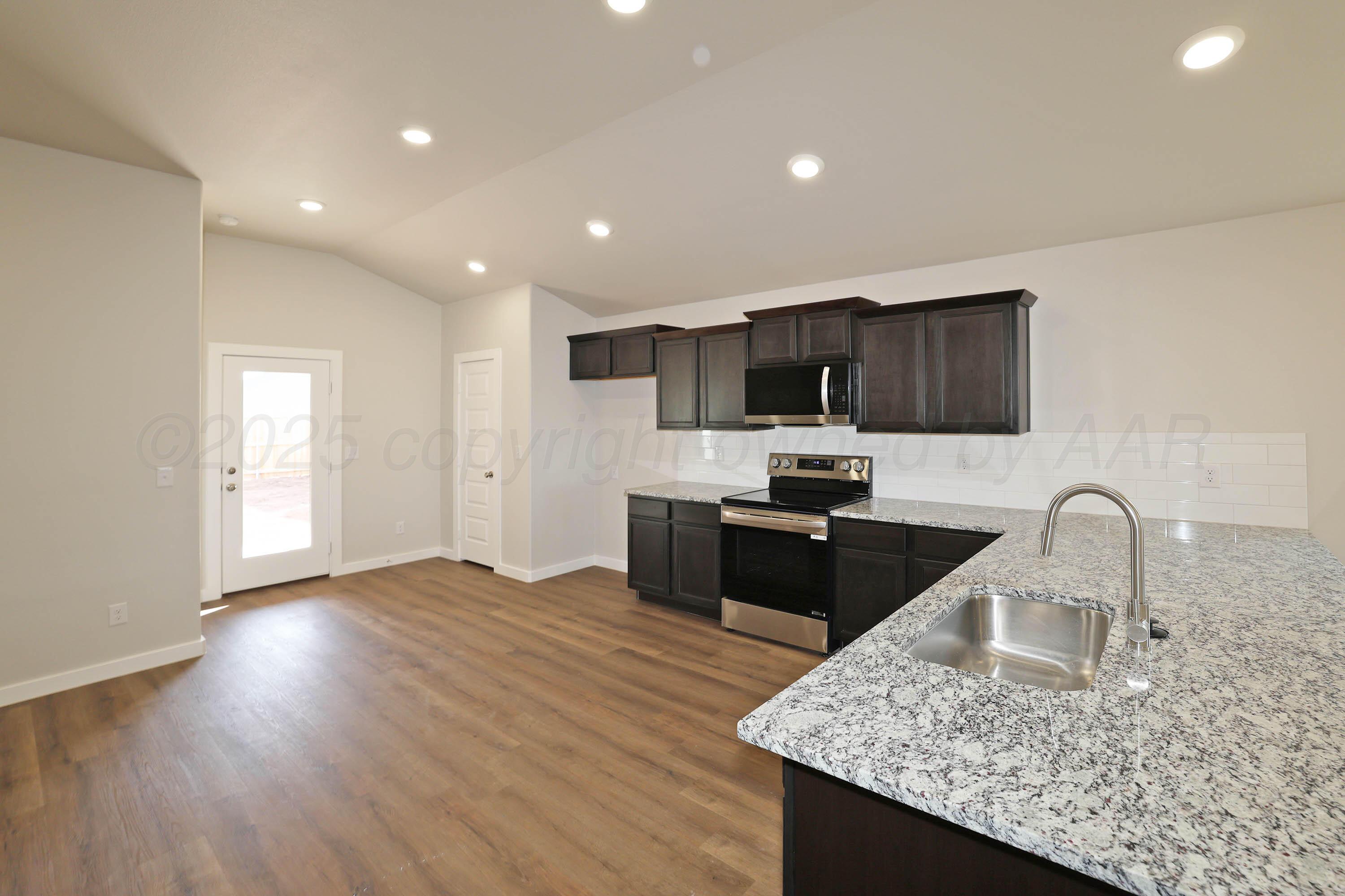 3003 Swenson Street Amarillo, TX 79124 - Photo 7 of 23 a kitchen with stainless steel appliances granite countertop a sink a stove top oven a refrigerator with wooden floors and cabinets