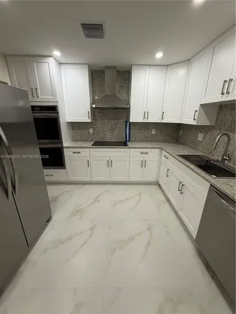 a large kitchen with stainless steel appliances granite countertop a stove a sink a refrigerator and white cabinets