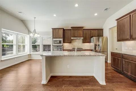 a kitchen with stainless steel appliances granite countertop a sink a stove a refrigerator cabinets and wooden floor