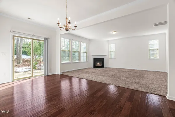 an empty room with wooden floor chandelier and windows