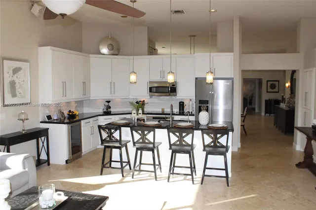 a kitchen with stainless steel appliances kitchen island granite countertop a dining table chairs and a refrigerator