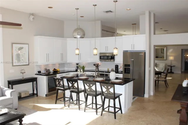 a kitchen with stainless steel appliances kitchen island granite countertop a dining table chairs and a refrigerator