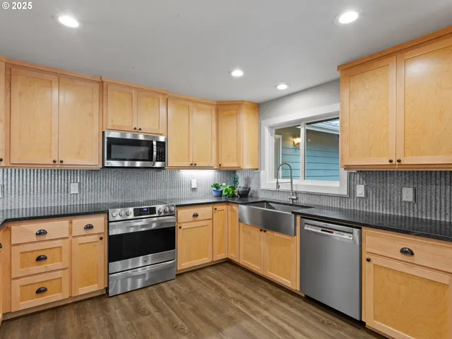 a kitchen with stainless steel appliances granite countertop a stove top oven a sink dishwasher and white cabinets with wooden floor