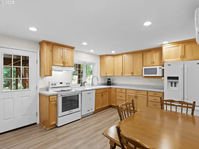 a kitchen with stainless steel appliances granite countertop a stove top oven a sink dishwasher a dining table and chairs with wooden floor