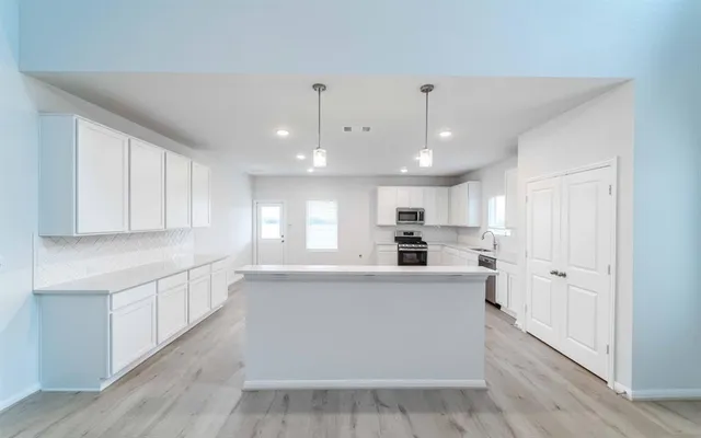 a large white kitchen with kitchen island a sink a center island and stainless steel appliances