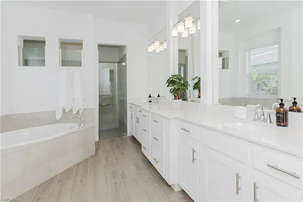 a spacious en suite bathroom with a double vanity sink a large mirror and a bathtub