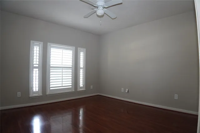 an empty room with wooden floor chandelier fan and windows