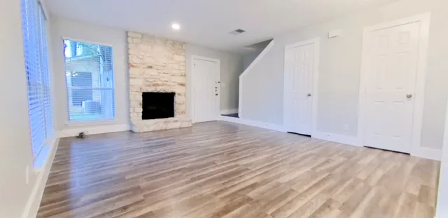 an empty room with wooden floor fireplace and windows