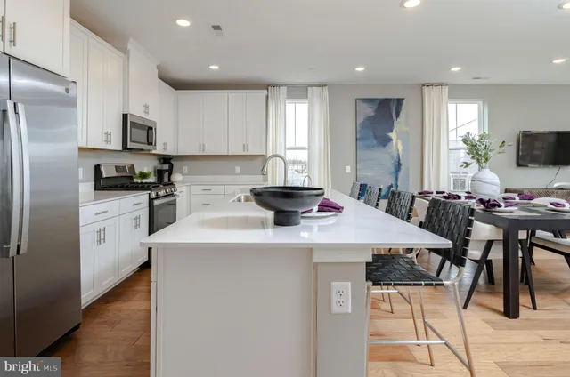 a kitchen with stainless steel appliances kitchen island granite countertop a sink a stove a refrigerator cabinets and a dining table with wooden floor