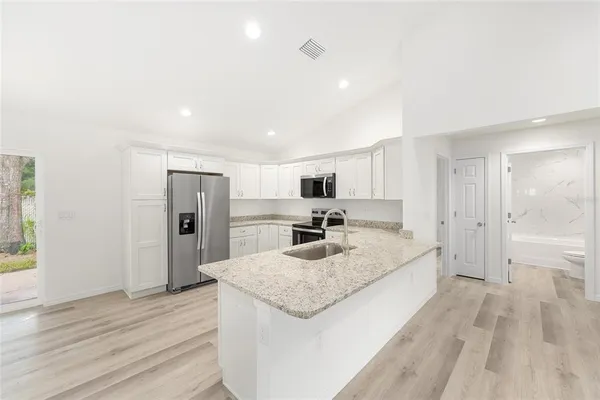 a large kitchen with kitchen island a sink dishwasher a refrigerator and a stove with wooden floor