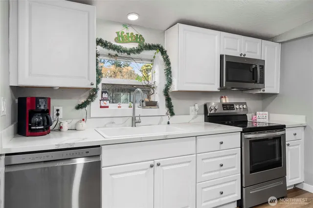 a kitchen with stainless steel appliances granite countertop a sink dishwasher a microwave oven and white cabinets with wooden floor