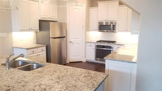 a kitchen with stainless steel appliances granite countertop a refrigerator a stove and a sink with wooden floor