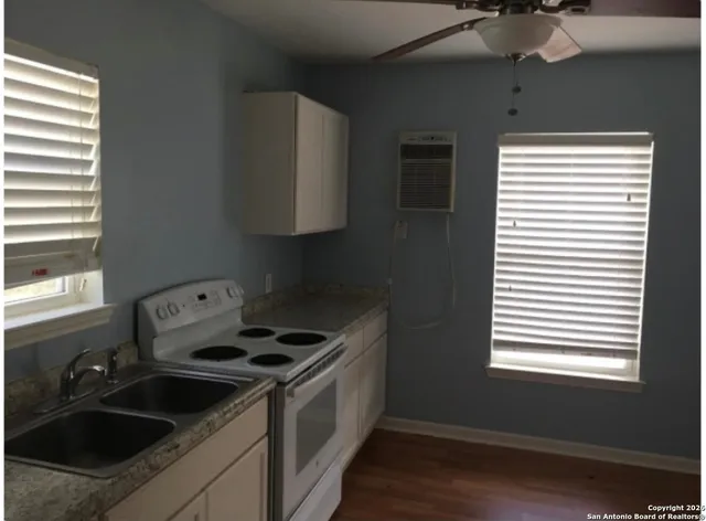 a area with wooden floor a ceiling fan and kitchen space
