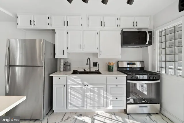 a kitchen with stainless steel appliances granite countertop a refrigerator a stove a sink a microwave oven with white cabinets and wooden floor