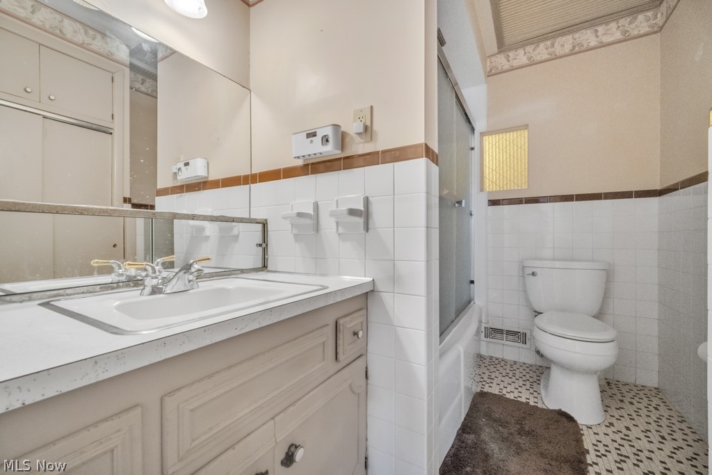 6846 Revere Road Cleveland, OH 44130 - Photo 18 of 30 Bathroom featuring vanity, shower / bath combination with glass door, tile walls, wainscoting, and tile patterned flooring