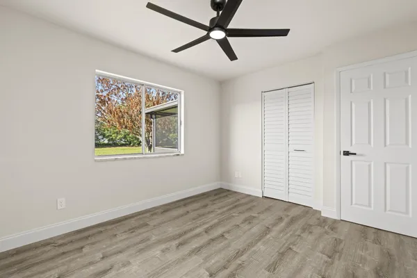 an empty room with wooden floor ceiling fan and windows