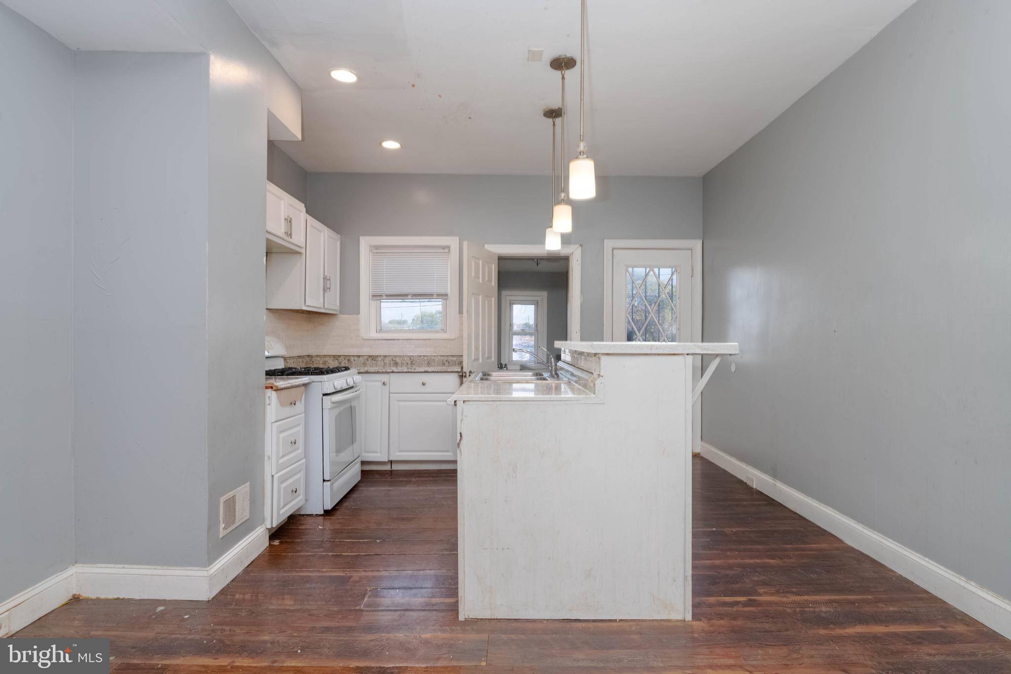 2216 West Fayette Street Baltimore, MD 21223 - Photo 9 of 36 a large white kitchen with a refrigerator a sink dishwasher a stove and white cabinets with wooden floor