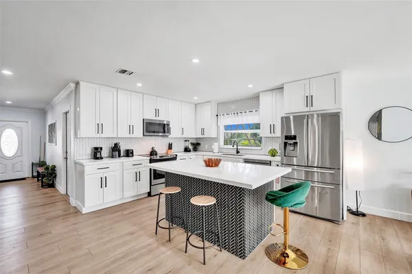 a kitchen with kitchen island granite countertop stainless steel appliances a sink a stove a refrigerator cabinets and wooden floor