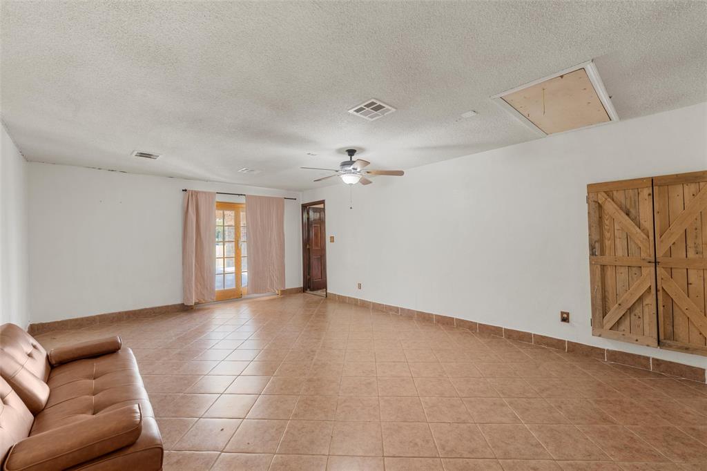 3433 West Tours Road West, TX 76691 - Photo 32 of 40 Unfurnished living room with attic access, a textured ceiling, light tile patterned flooring, and a ceiling fan