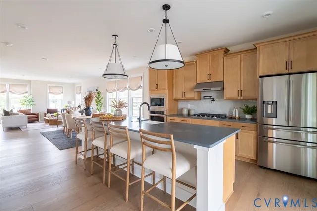 a kitchen with stainless steel appliances granite countertop a refrigerator a stove a sink dishwasher a dining table and chairs with wooden floor