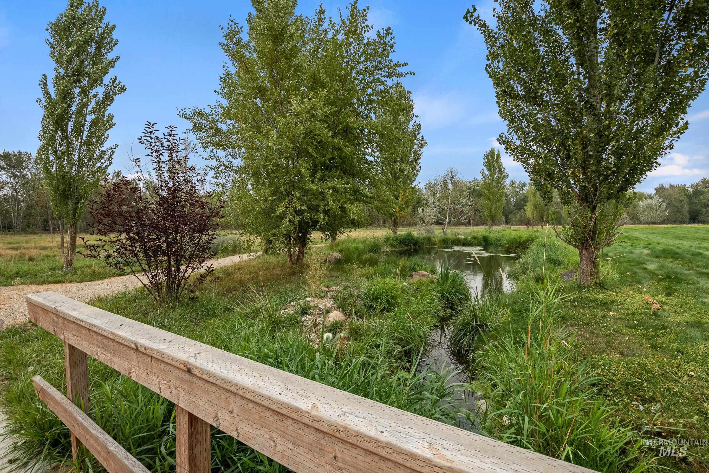 939 South Lake Pointe Way Eagle, ID 83616 - Photo 40 of 50 Wood railing with a natural finish, overlooking a serene pond surrounded by tall grasses and mature trees