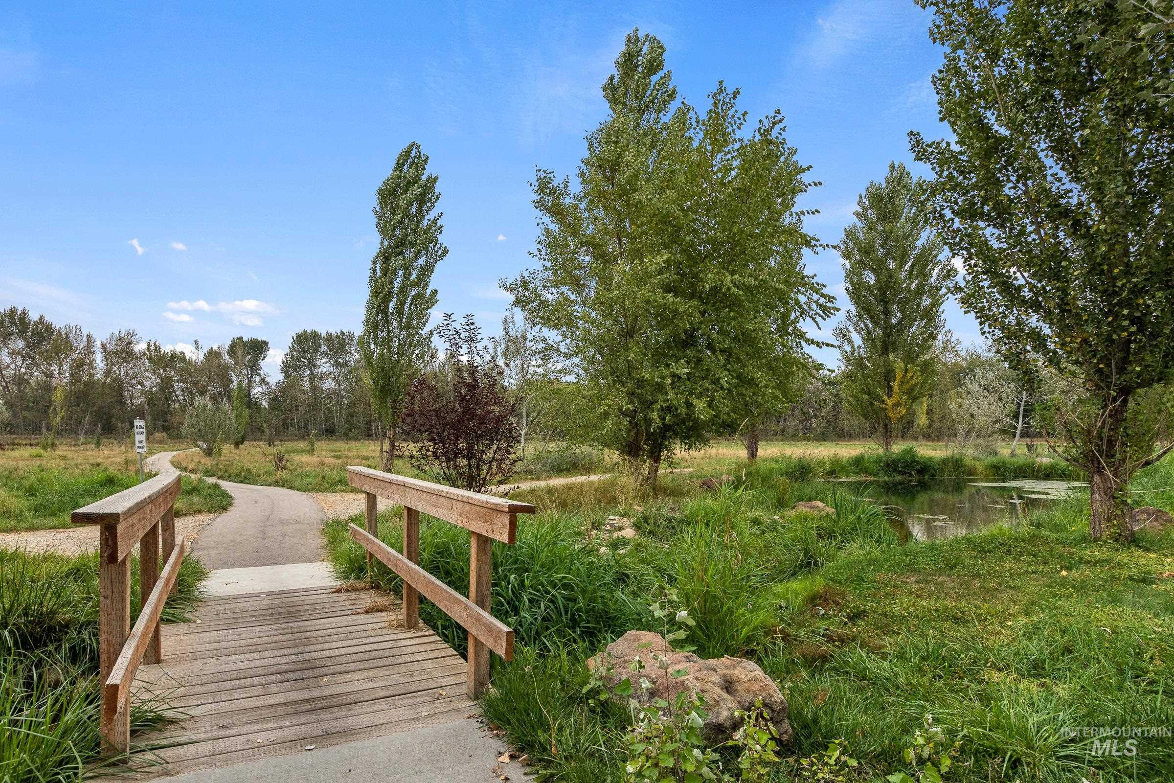 939 South Lake Pointe Way Eagle, ID 83616 - Photo 41 of 50 Wood footbridge over a natural water feature, surrounded by mature trees, varied green foliage, and a winding pathway