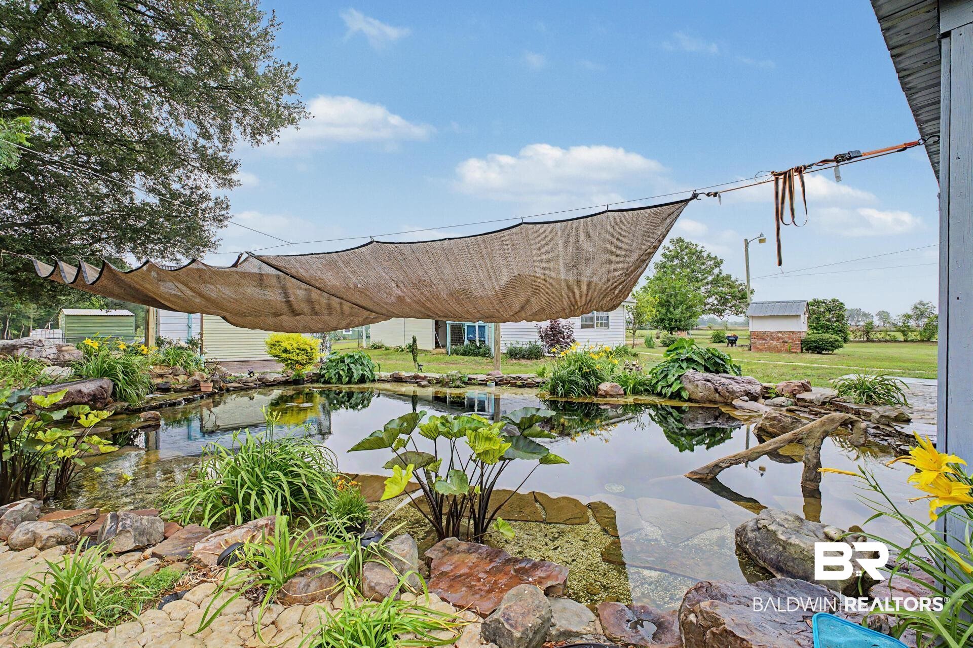 3791 Robinsonville Road Atmore, AL 36502 - Photo 18 of 47 Outdoor pond area featuring a water feature, rock landscaping, mature plantings, and a shade sail structure