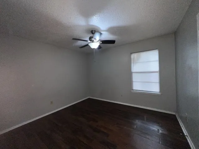 an empty room with wooden floor fan and windows