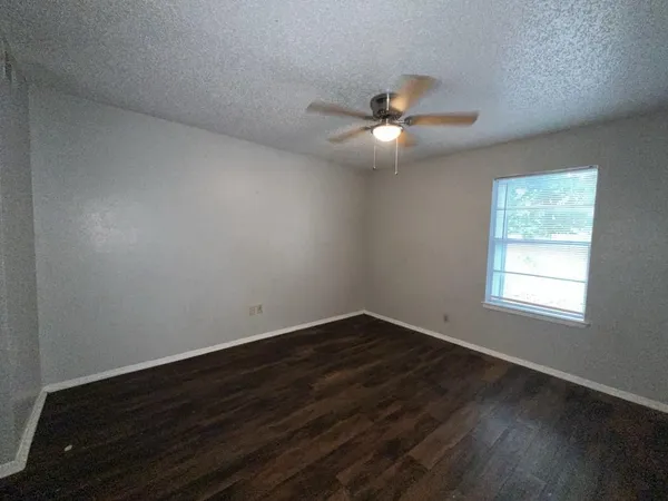 an empty room with wooden floor fan and windows