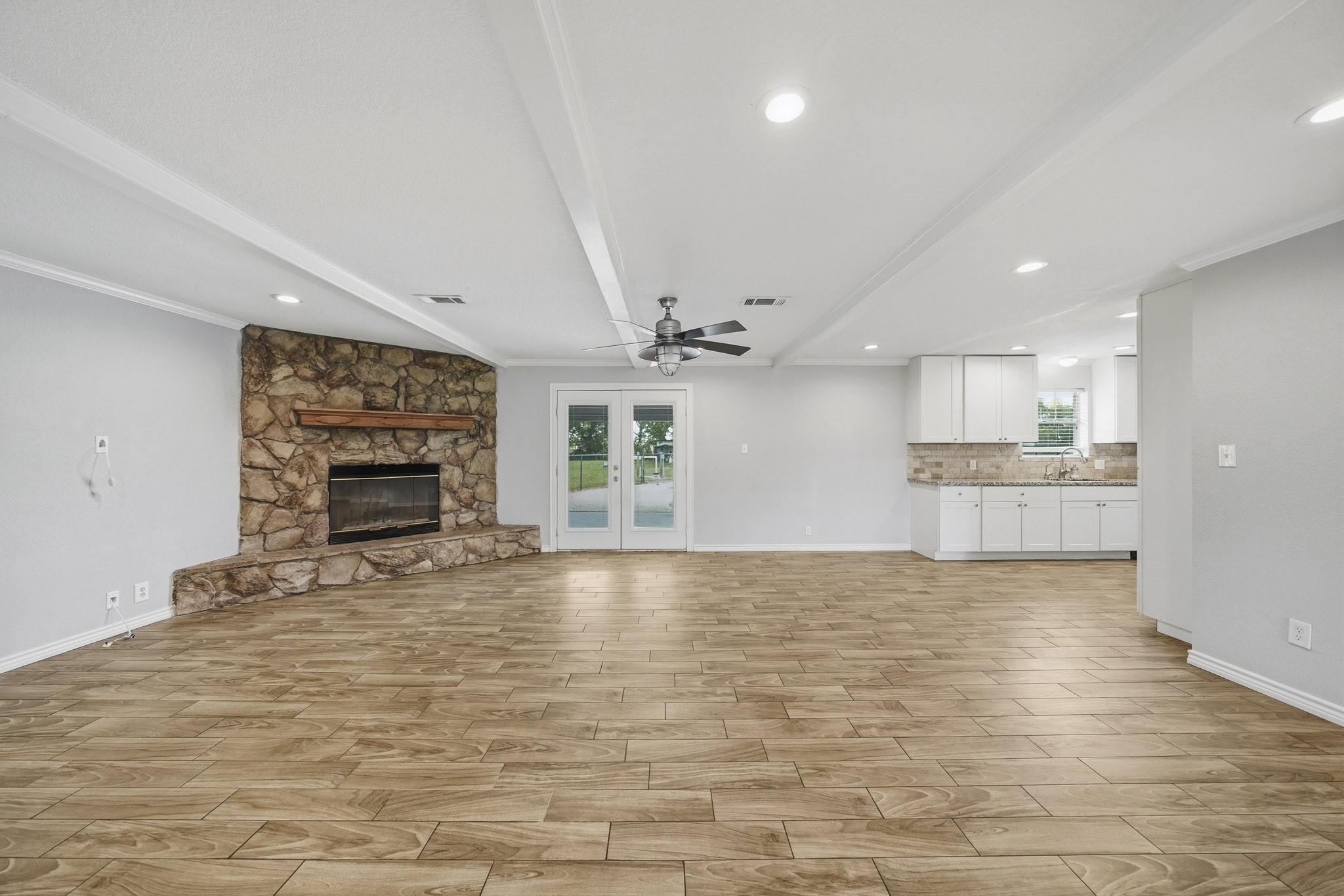 302 Country Road 893 Angleton, TX 77515 - Photo 10 of 26 This spacious open-concept living area features a stone fireplace, modern ceiling fan, and light wood-look flooring. It seamlessly connects to a bright kitchen with white cabinetry and tile backsplash, offering a welcoming and versatile space.