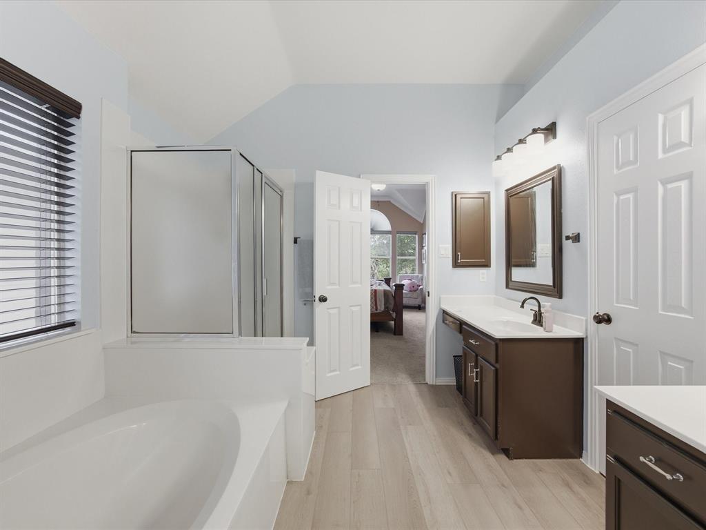 4008 Falcon Ridge Drive Haltom City, TX 76137 - Photo 26 of 40 Primary Bathroom featuring wood-finish flooring, a built-in soaking tub, a stand-up shower with a glass enclosure, and a vanity with a white countertop