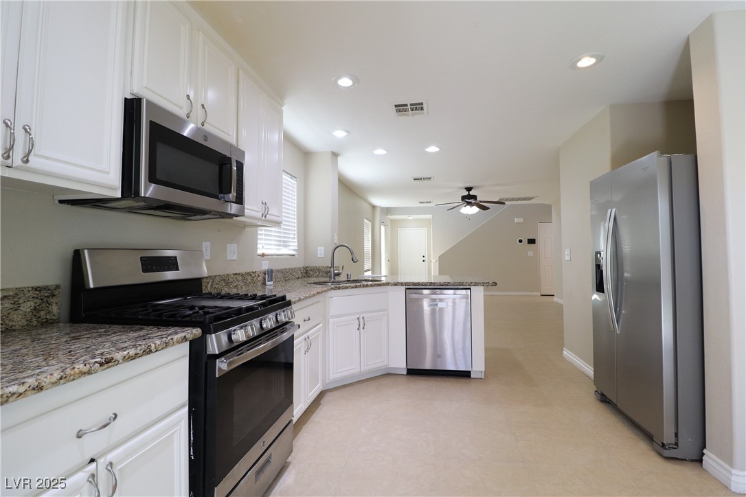 8708 Palomino Ranch Street Las Vegas, NV 89131 - Photo 2 of 19 Kitchen featuring appliances with stainless steel finishes, a peninsula, white cabinets, light stone counters, and recessed lighting