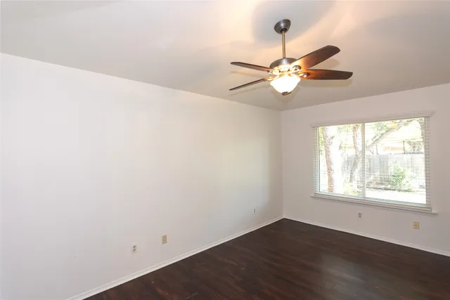 an empty room with wooden floor chandelier fan and windows