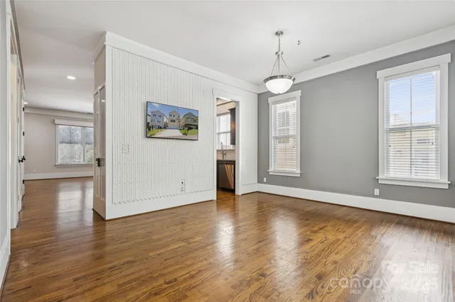 an empty room with wooden floor and way to kitchen