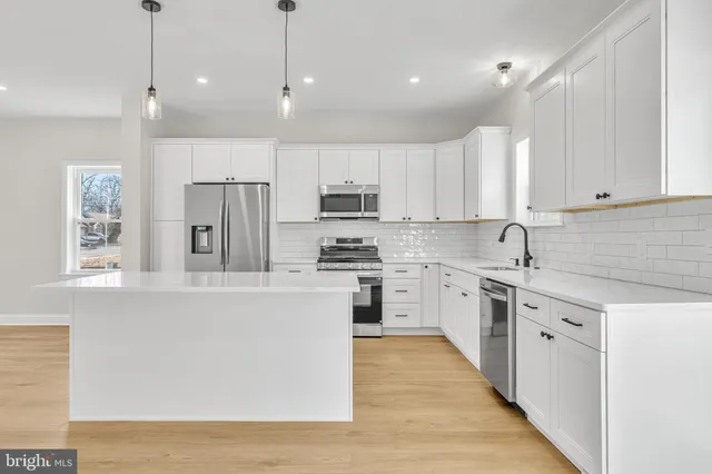 a kitchen with stainless steel appliances granite countertop a stove a sink a refrigerator and white cabinets with wooden floor