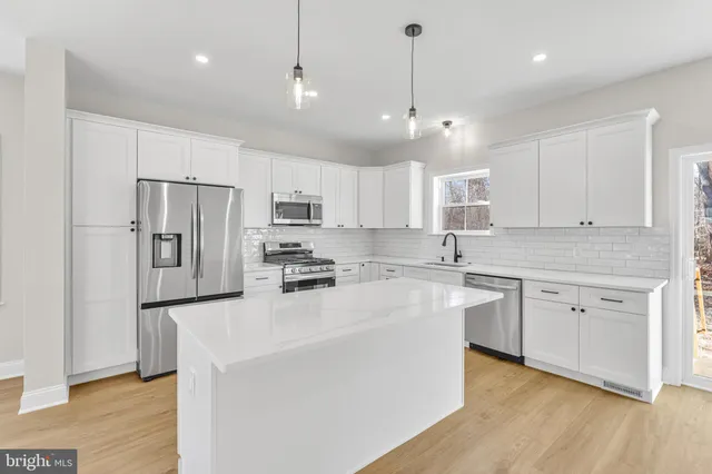 a kitchen with stainless steel appliances granite countertop a refrigerator a sink dishwasher a oven and white cabinets with wooden floor