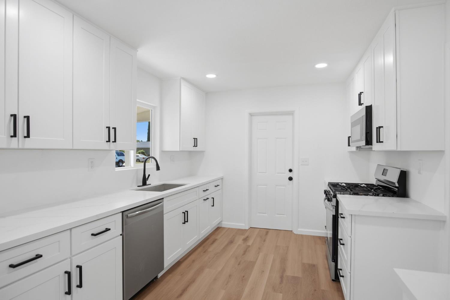 1451 Kent Way Modesto, CA 95355 - Photo 12 of 37 a kitchen with white cabinets a sink dishwasher and a stove with wooden floor