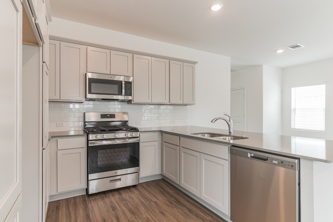 231 Rioja Kyle, TX 78640 - Photo 10 of 29 Kitchen featuring stainless steel appliances, dark wood-type flooring, a peninsula, decorative backsplash, and light stone counters