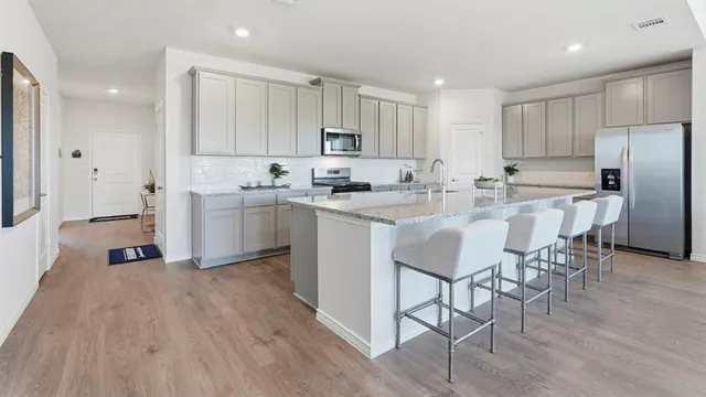 a kitchen with stainless steel appliances a stove a sink a refrigerator white cabinets and wooden floor