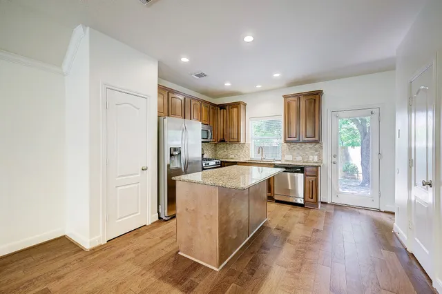 a kitchen with stainless steel appliances granite countertop a refrigerator a sink dishwasher and a stove with wooden floor