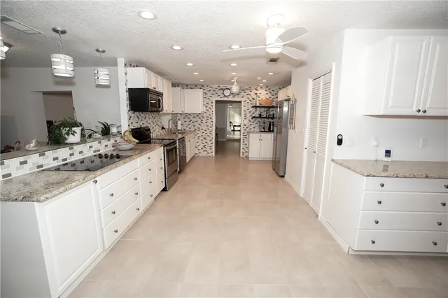 a large white kitchen with kitchen island a large counter space a sink stainless steel appliances and cabinets